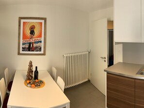 A small, modern kitchen with a white countertop and wooden cabinets. A framed poster hangs on the wall above the dining table, which has a white tablecloth and a small Christmas tree decoration. - Ferienwohnungen Soldanella, (Grächen), by Interhome (Grächen)