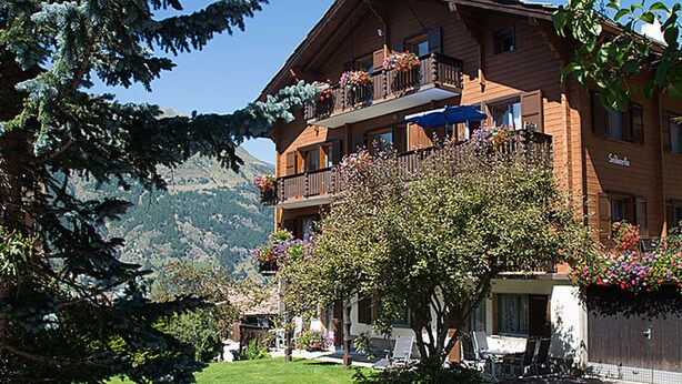 A two-story wooden building with balconies, surrounded by greenery and mountains. - Soldanella, (Grächen), by Interhome (Grächen)