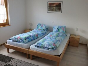 Un lit double avec une literie à motifs floraux, deux tables de chevet avec des lampes, un tableau encadré au mur et une fenêtre avec des rideaux.
