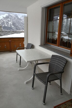 Ein Balkon mit Tisch und zwei Stühlen, einem Holzzaun und einem Fenster mit Spitzenvorhängen.