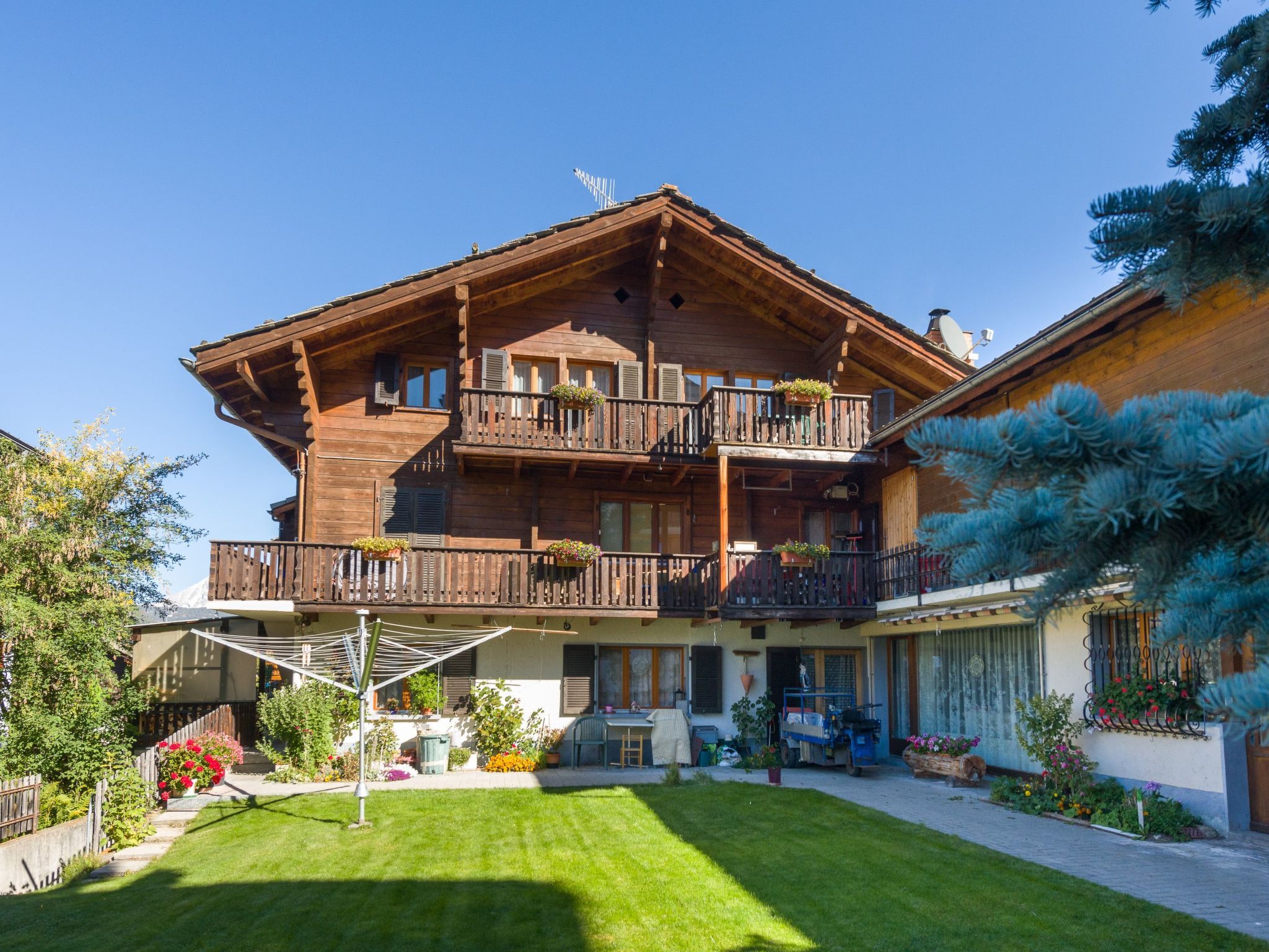 A two-story wooden chalet with balconies, a well-maintained lawn, and a satellite dish.