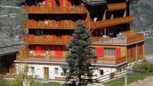 Un edificio de varios pisos con balcones, fachada de madera y montañas al fondo.