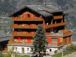 Ein mehrstöckiges Gebäude mit Balkonen, einer Holzfassade und einem Bergpanorama im Hintergrund.