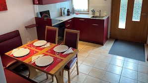 Una cocina compacta con armarios rojos, una mesa de comedor preparada para cuatro personas y una ventana pequeña.