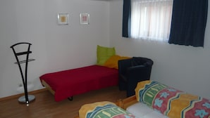 Un alojamiento pequeño de una sola habitación, con cama, una silla, mesita de noche y ventana con cortinas.