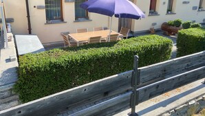 Un patio con una mesa y sillas, un paraguas morado y un seto.
