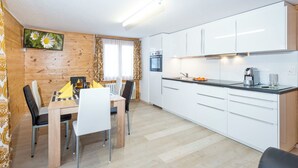 A modern kitchen with white cabinets, a dining area with a wooden table and chairs, and a sofa. - Ferienwohnungen Miranda, (Grächen), by Interhome (Grächen)