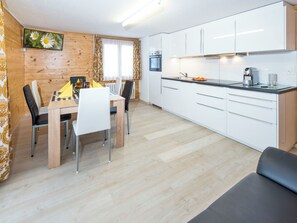 Eine moderne Küche mit weißen Schränken, ein Essbereich mit Holztisch und Stühlen sowie eine Sitzecke mit einer Couch.