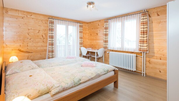 A wooden-paneled room with a bed, a desk, and a chair. - Ferienwohnungen Miranda, (Grächen), by Interhome (Grächen)