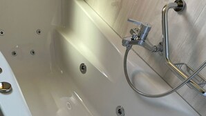 A bathtub with a shower head and hose, a drain, and a wall-mounted faucet. - Ferienwohnungen Miranda, (Grächen), by Interhome (Grächen)