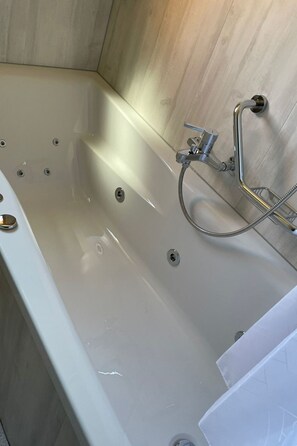 Eine Badewanne mit Duschkopf und Duschschlauch, einem Ablauf und einem am Wand montierten Wasserhahn.