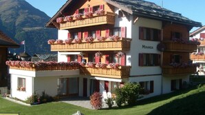 A multi-story hotel with balconies adorned with flowers, set against a mountainous backdrop. - Ferienwohnungen Miranda, (Grächen), by Interhome (Grächen)