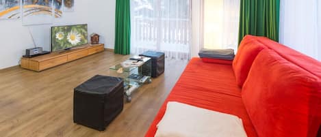 A modern living room with a red sofa, a glass coffee table, and a wooden TV stand.