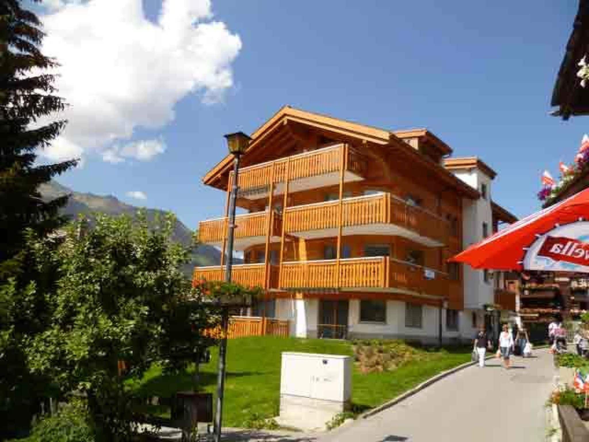A multi-story building with balconies, a clear sky, and a mountain in the background.
