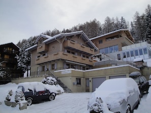 A multi-story building with balconies, a ski lift, and snow-covered surroundings. - Steinbock, (Grächen), 2024 by Interhome (Grächen)