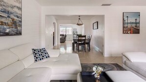 A modern living room with a white sofa, a coffee table, and a dining area in the background. - Tropical Bliss Retreat: Poolside Paradise Awaits (Pembroke Pines)