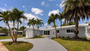 A modern two-story house with a paved driveway, palm trees, and a clear blue sky. - Tropical Bliss Retreat: Poolside Paradise Awaits (Pembroke Pines)