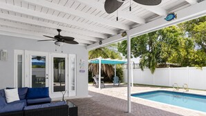 A covered patio area with a pool, a blue sofa, and a ceiling fan. - Tropical Bliss Retreat: Poolside Paradise Awaits (Pembroke Pines)