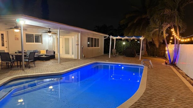 A swimming pool with a covered patio area, a dining table, and chairs. - Tropical Bliss Retreat: Poolside Paradise Awaits (Pembroke Pines)