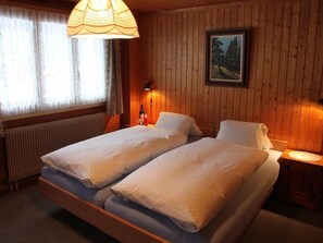 A double bed with a wooden headboard, a bedside table with a lamp, and a framed picture on the wall. - Ferienwohnungen Bel Air, (Grächen), 1292 & 1575 by Interhome (Grächen)