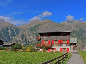 Ein zweistöckiges Gebäude mit Balkon, eingebettet in eine gebirgige Landschaft.