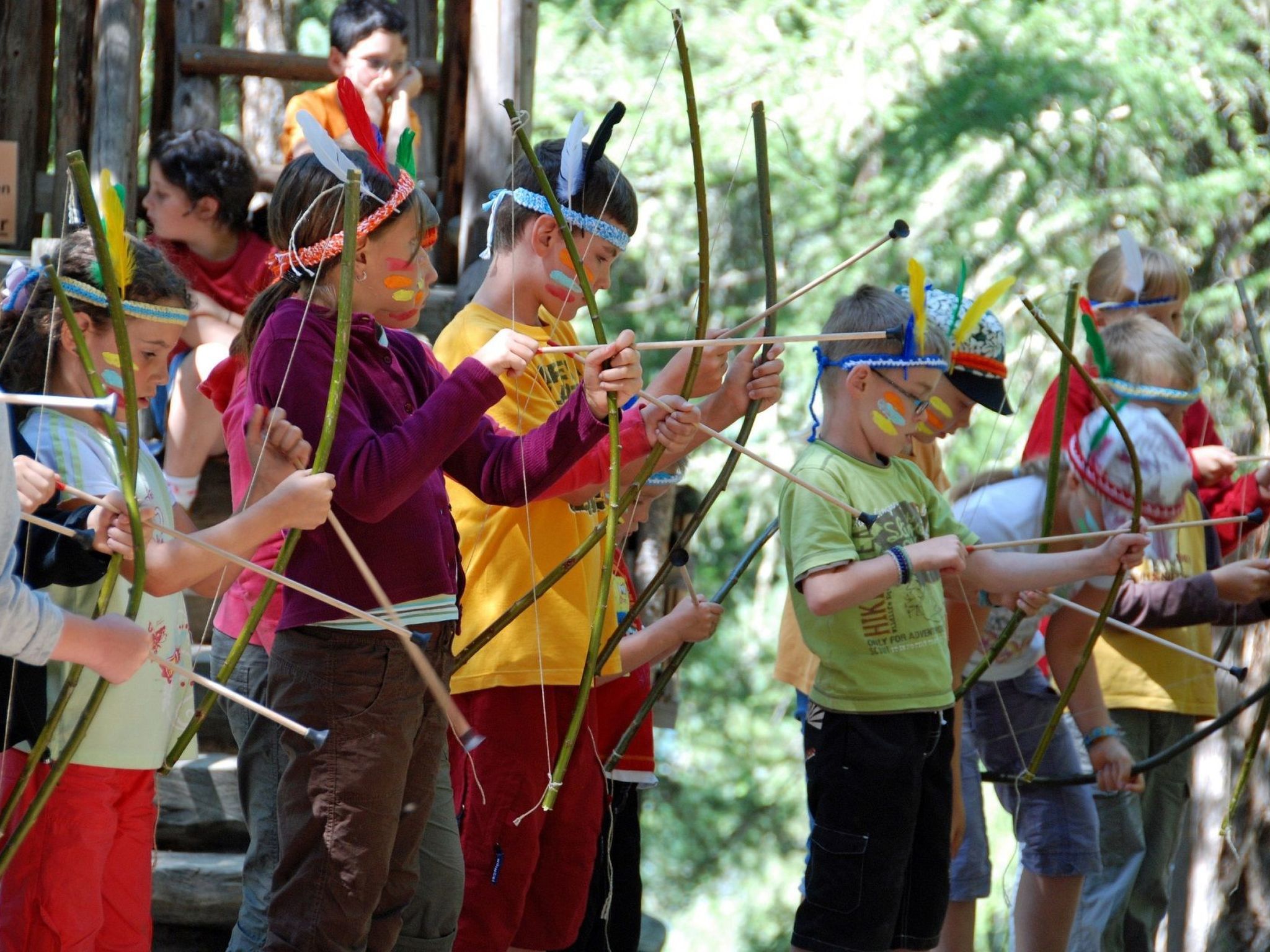 Un grupo de niños participa en una actividad al aire libre, posiblemente tiro con arco, en un área boscosa.