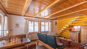 A cozy living room with a wooden ceiling, a dining area with a table and chairs, a sofa, a fireplace, and a television. - Dominique, (Grächen), 1013 by Interhome (Grächen)