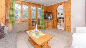 Un interno in legno con un divano, un tavolo, un televisore e vista sulle montagne attraverso ampie finestre.