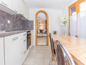A modern kitchen with white cabinetry, a wooden countertop, and a dining area with a wooden table and chairs. - Ferienwohnungen Bergfink, (Grächen), 1190-1199 by Interhome (Grächen)