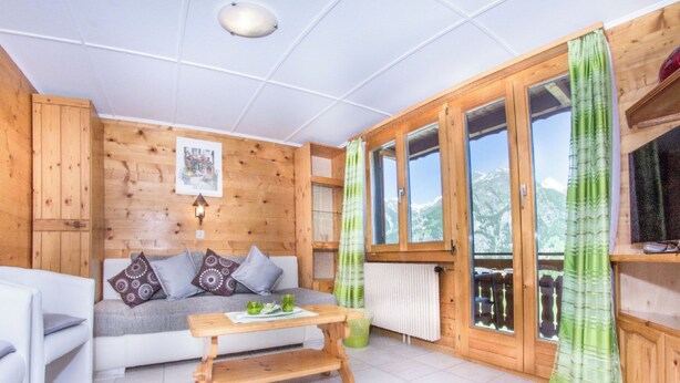 Interno di una baita in legno con divano, tavolo e finestra vista montagne.