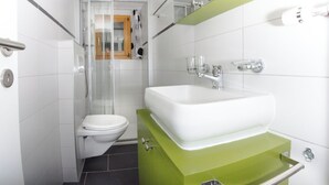 Un bagno con il water, uno spazio doccia, un lavandino e uno specchio.