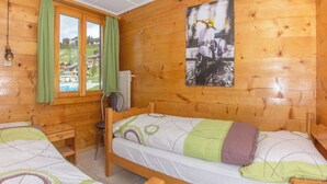 Una camera in una casetta di legno con due letti, una finestra con tende, un termosifone e un quadro appeso al muro.