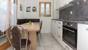 Una cucina compatta con tavolo, sedie, forno a incasso e finestra con tende.