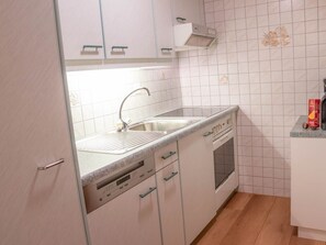 Una cocina con armarios blancos, un lavamanos de acero inoxidable, horno empotrado y microondas.