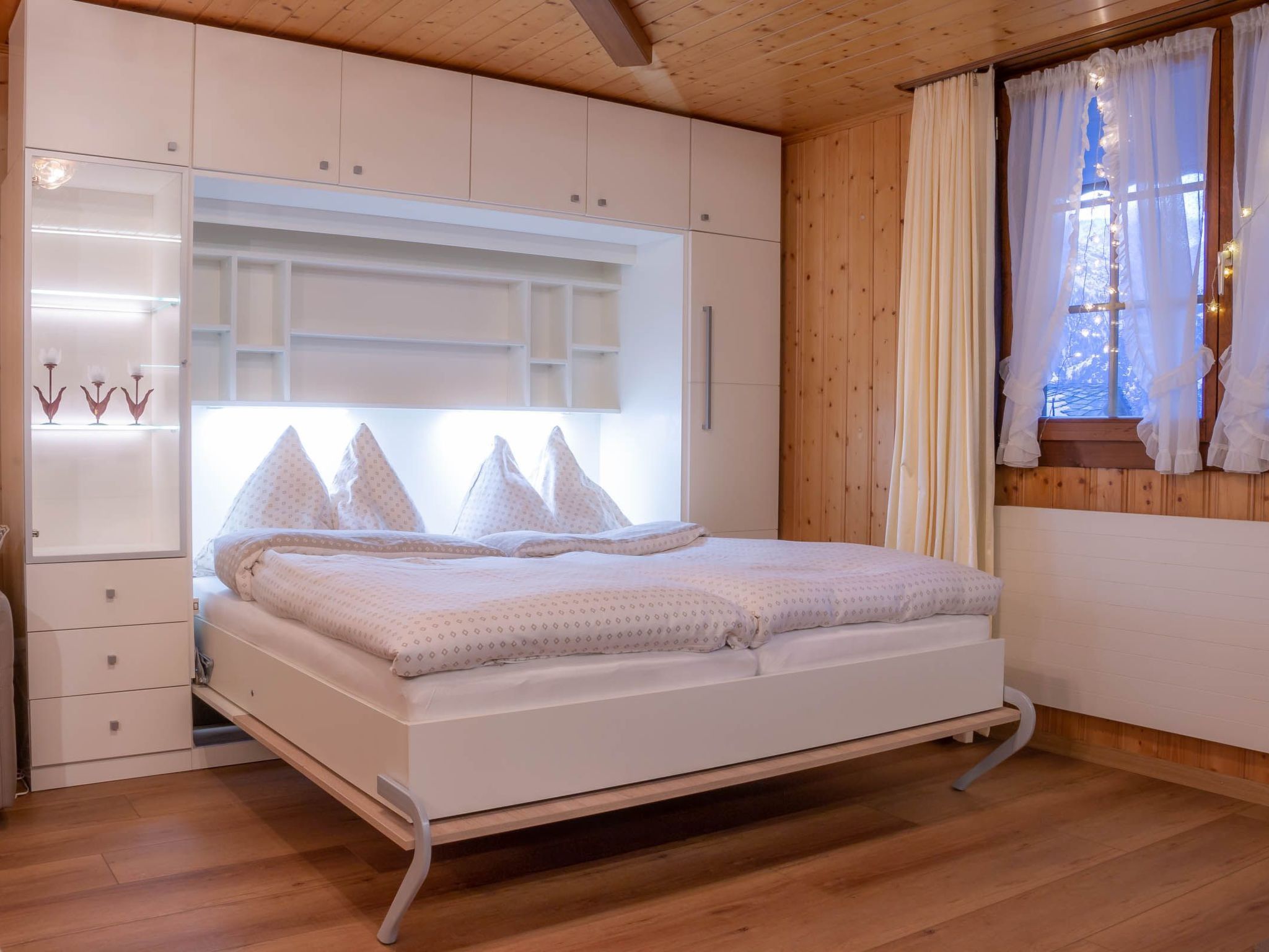A bedroom with a bed, built-in wardrobe, and a window with curtains.