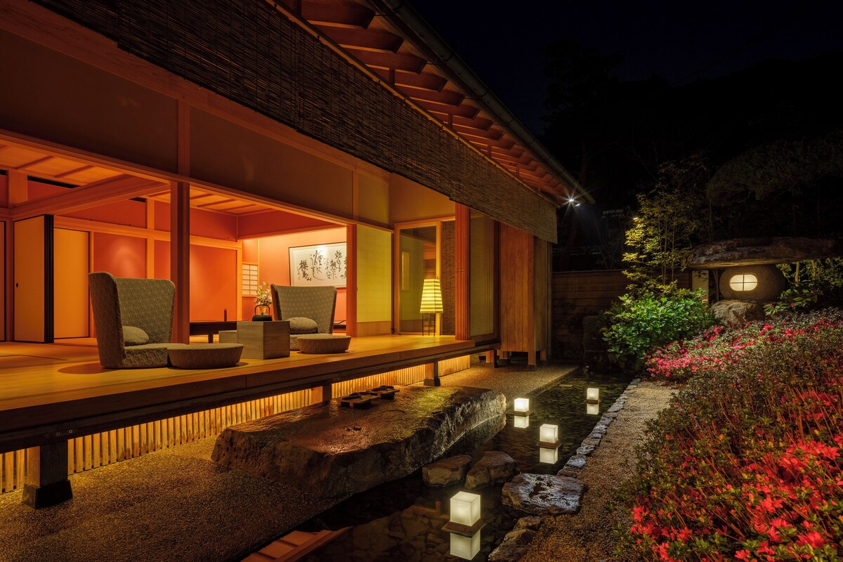 Un edificio de estilo japonés tradicional con pisos de tatami, una terraza de madera y un estanque de carpas koi.