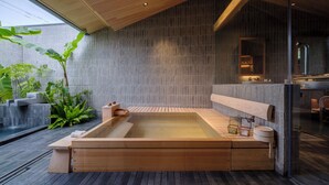 Un spa moderne doté d’un bain à remous en bois, d’un mur en pierre et d’une grande fenêtre donnant sur un paysage verdoyant.