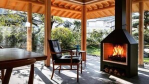 A cozy room with a fireplace, wooden ceiling beams, and large windows. - Hogetsu (Kagoshima)