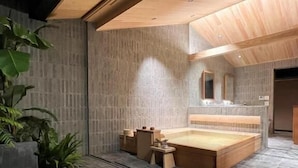 A modern bathroom with a large bathtub, a wooden ceiling, and a stone floor. - Hogetsu (Kagoshima)