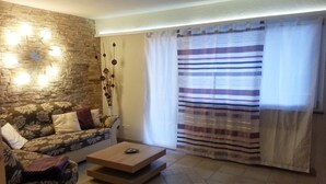 Un salon avec un canapé, une table basse, un mur en pierre et une fenêtre avec des rideaux.