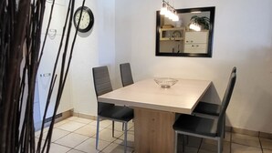 Un coin repas comprenant une table rectangulaire, quatre chaises, une horloge murale et un luminaire suspendu.