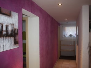 Ein Flur mit einer rosafarbenen Wand, einer zur einem Zimmer führenden Tür und einem Fenster mit Blick.