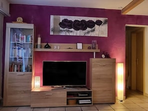 A living room with a TV, bookshelf, and decorative items on the wall. - Ferienwohnungen Silberblick, (Grächen), by Interhome (Grächen)