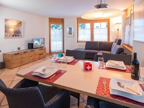 Un comedor con una mesa dispuesta para dos, un sofá y un televisor al fondo.