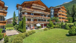 Ein mehrstöckiges Hotel mit Balkonen, einem Garten und einer Bergkulisse.