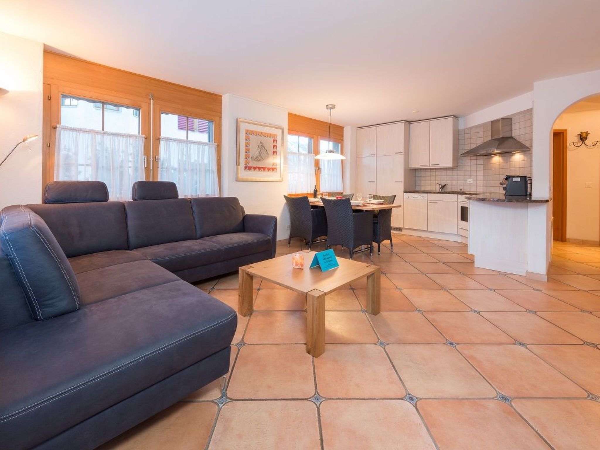 Een moderne woonkamer met een bank, een eettafel en een keuken met kastjes en een fornuis.