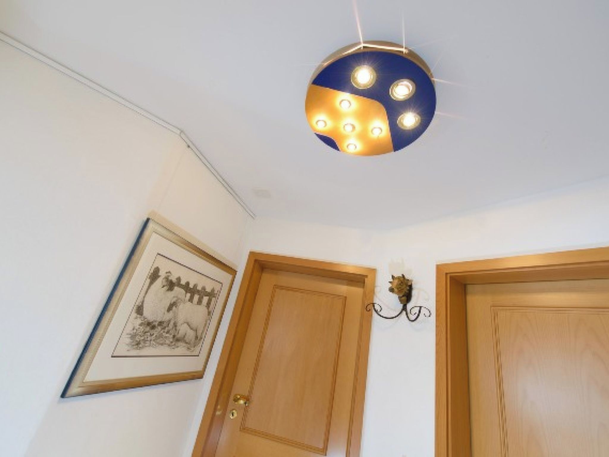 Ein Zimmer mit einer Deckenleuchte, zwei Holztüren und einem gerahmten Bild an der Wand.