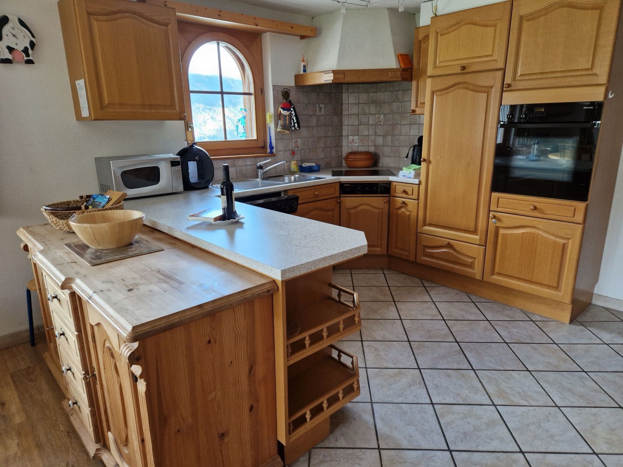A kitchen with wooden cabinets, a microwave, a sink, and a large window.
