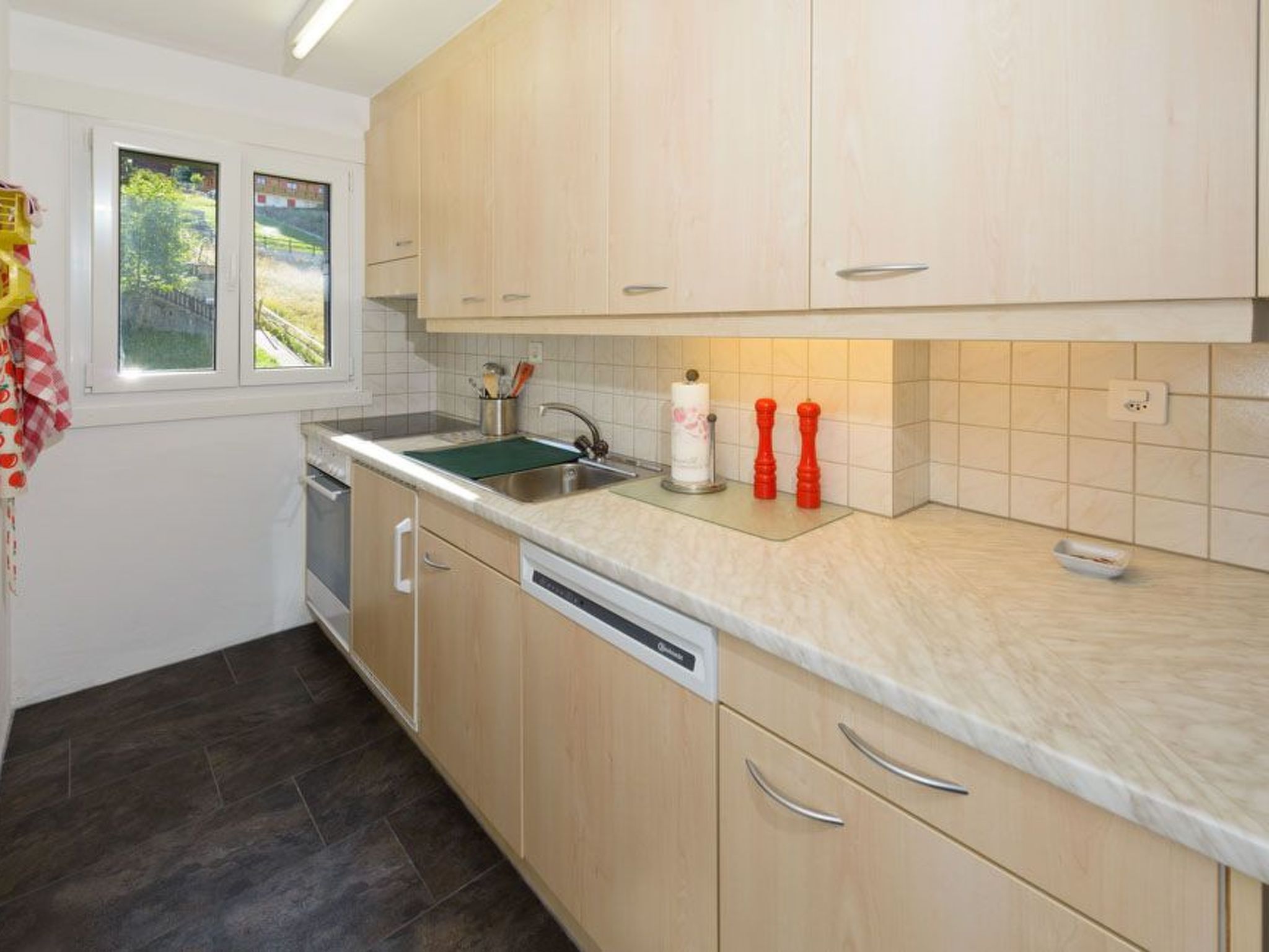 A kitchen with a dishwasher, a sink, and a window with a view of greenery.
