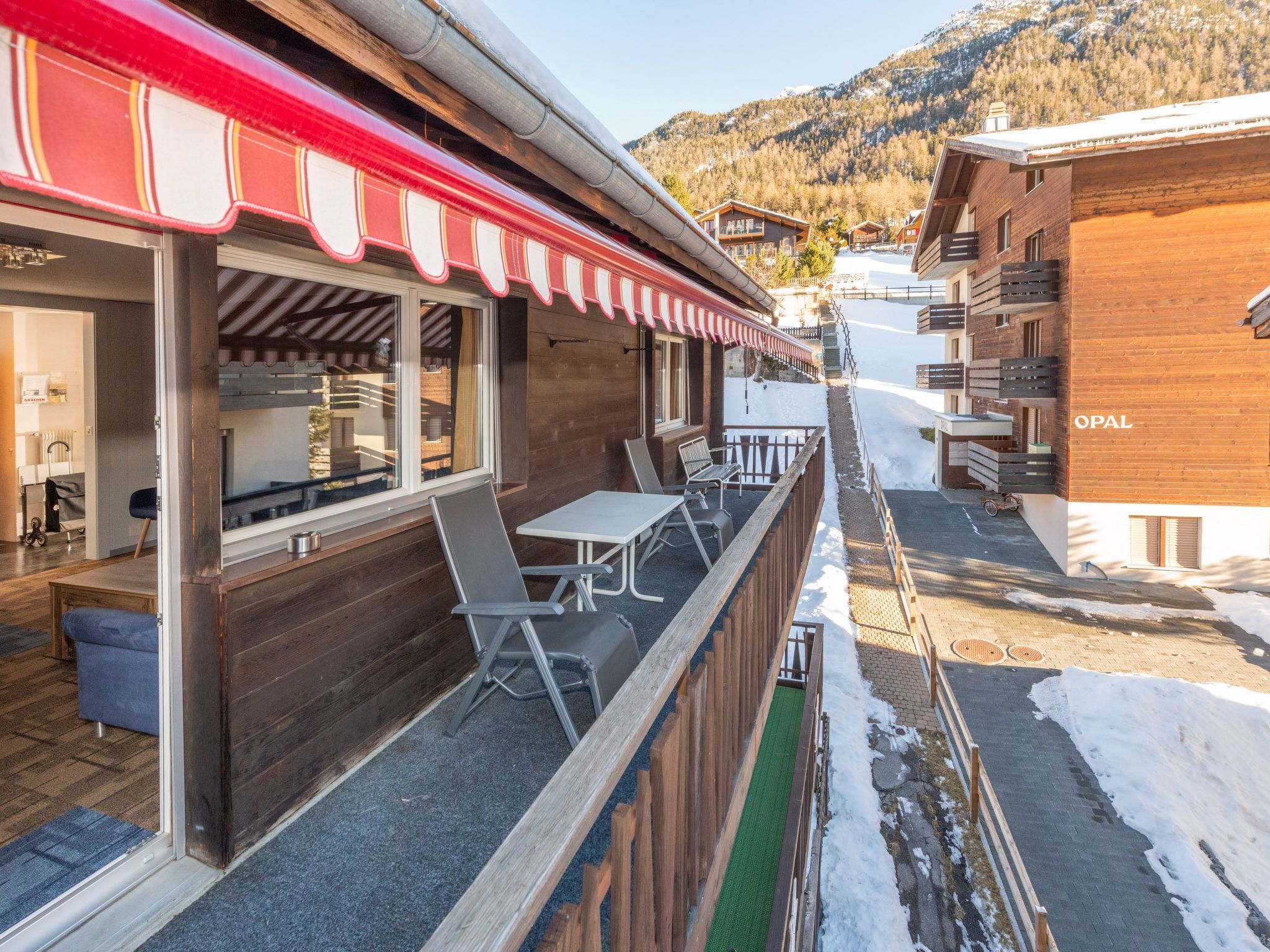 A wooden building with a red awning, outdoor seating, and a view of snow-covered mountains.